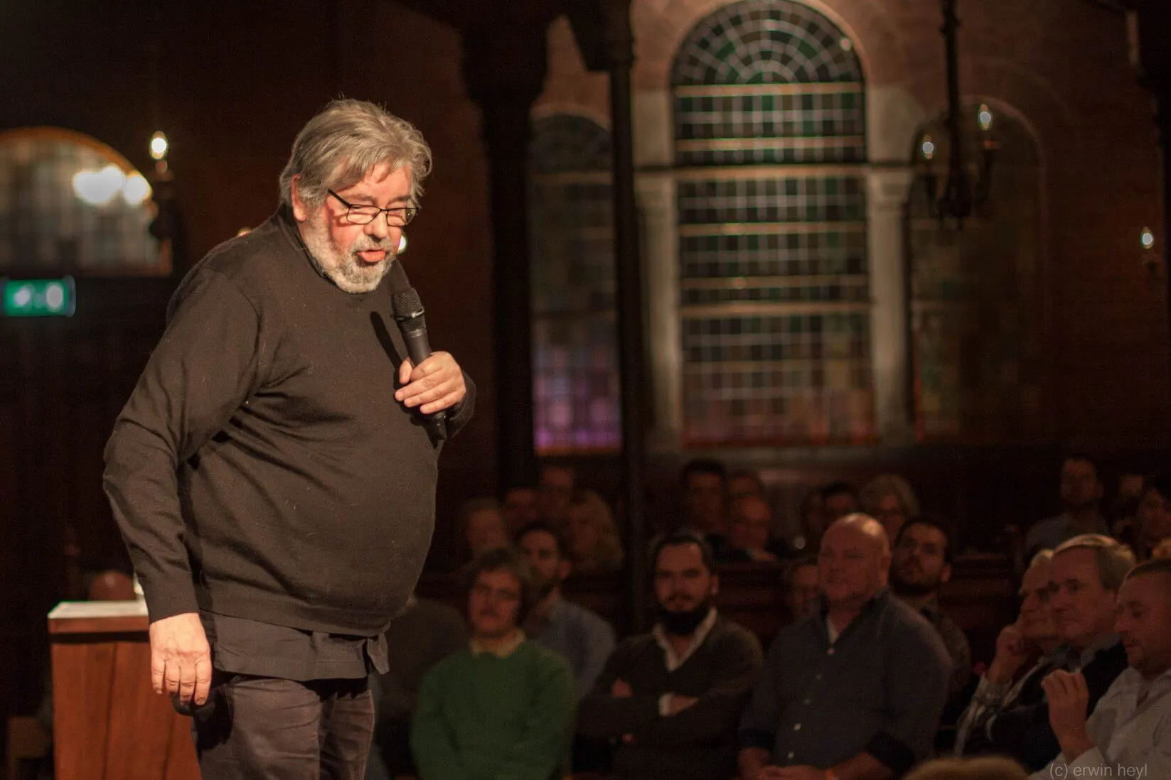 Spreker met microfoon voor publiek in de warme zaal van Arminius