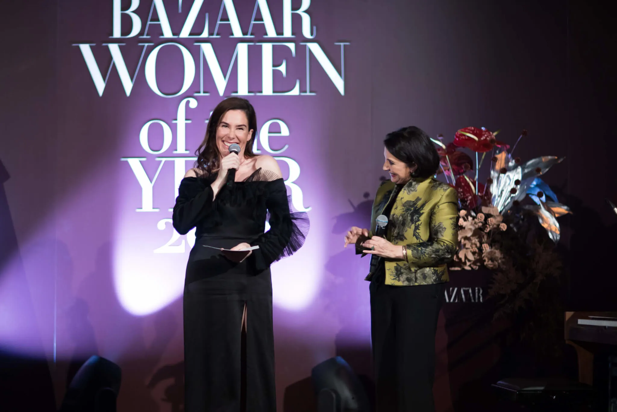 Twee presentatoren op het uitgelichte podium voor de Women of the Year-backdrop